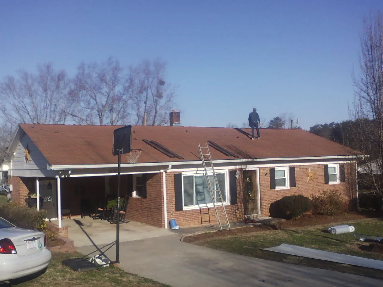 Roofer stripping a shingle roof on a brick ranch before metal panels in West Fork