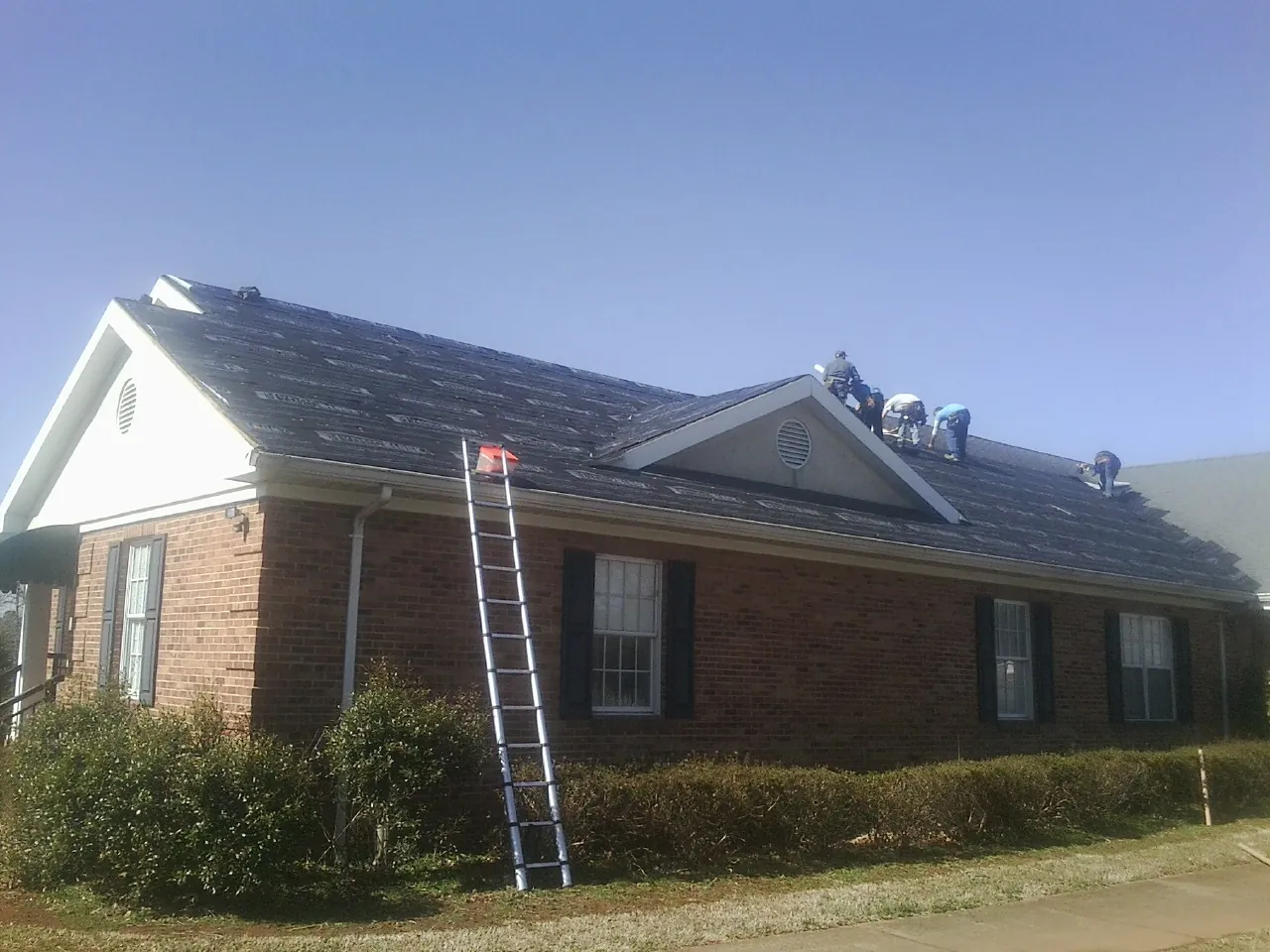 Crew tearing shingles off a brick ranch roof with a ladder set — Emergency Roof Repair work by our crew in West Fork