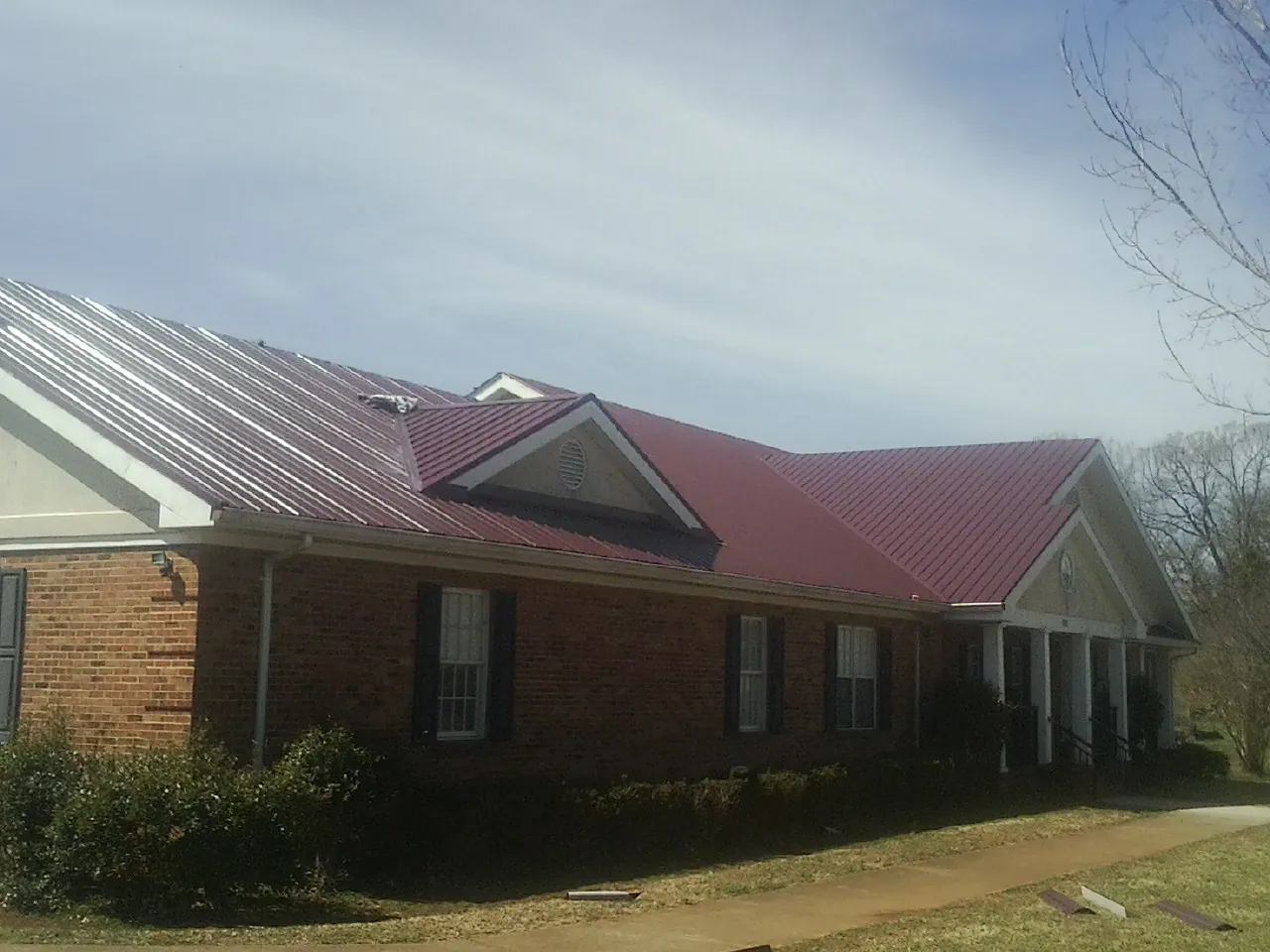 Red metal roof with gabled entries on a long brick building, from a Hail Damage Roof Repair job in West Fork
