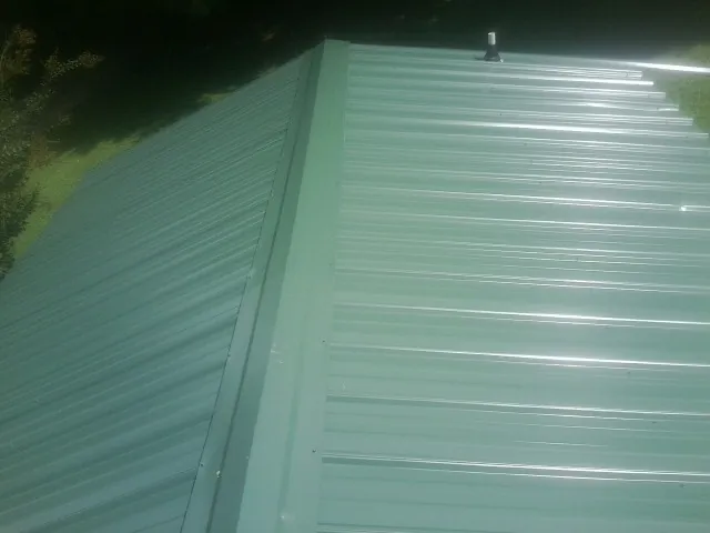 New green metal panels meeting at the ridge of a roof — Flat Roof Repair work by our crew in West Fork