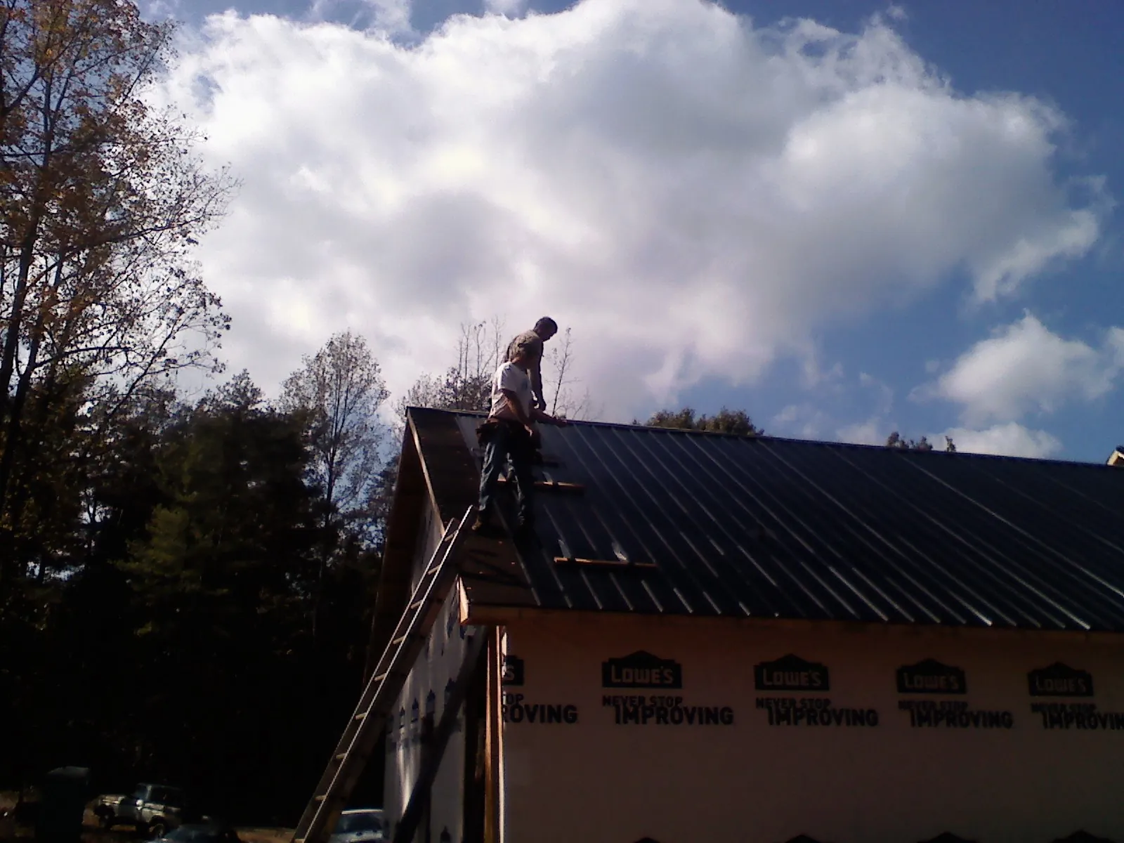 Roofer fastening dark metal panels high against a cloudy sky, from a Roof Inspection job in West Fork