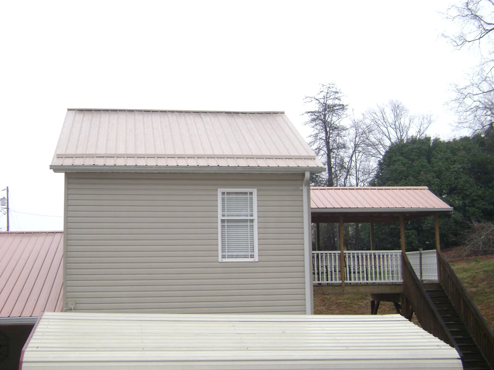 Tan metal roofs on a two story addition and attached porch, from a Roof Replacement job in West Fork